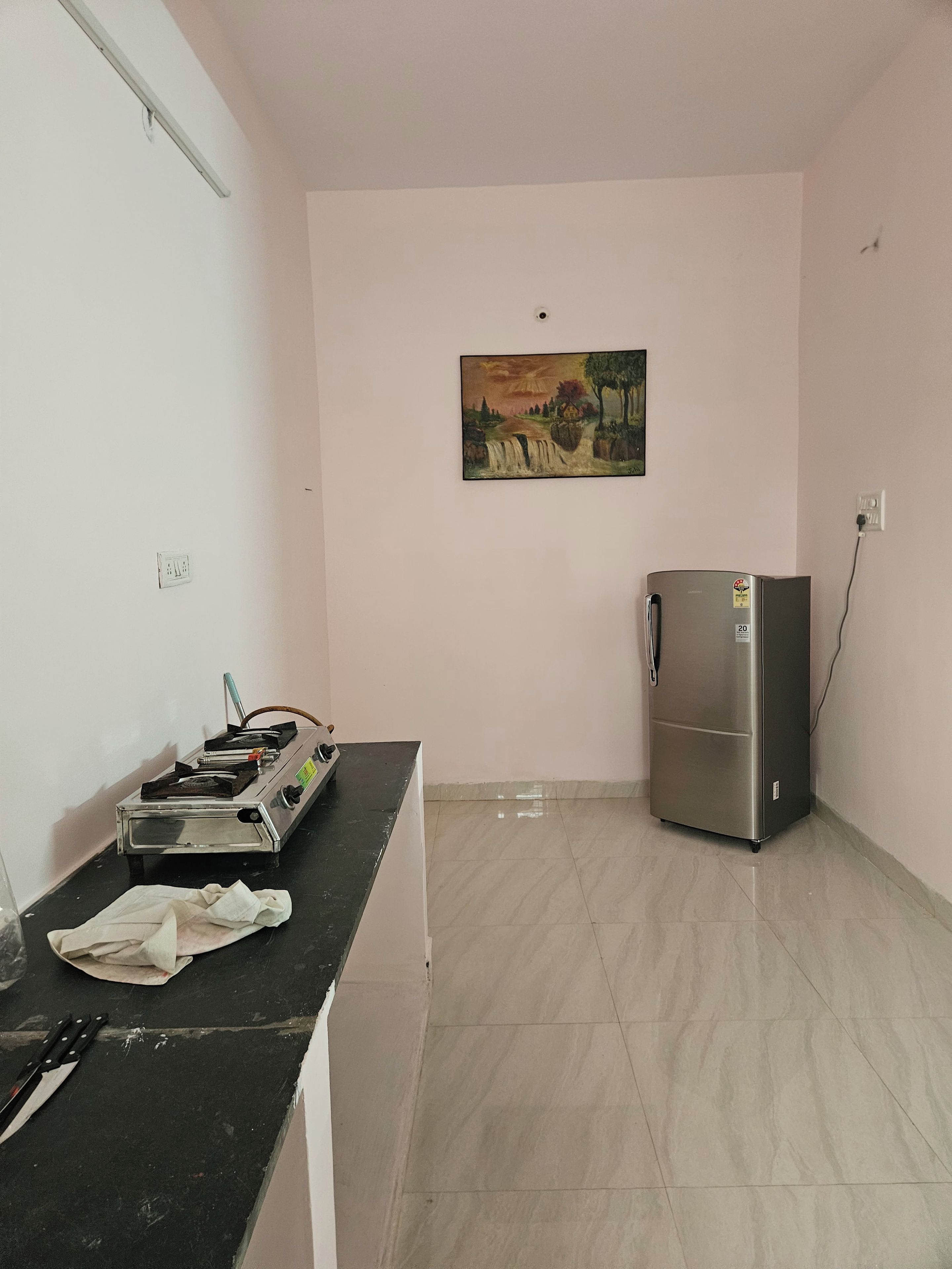 A kitchen with a refrigerator, a gas stove, and a painting on the wall.