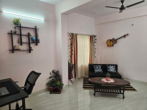Sala de estar com sofá, mesa de centro, um laptop em uma escrivaninha, guitarra na parede e ventilador de teto.