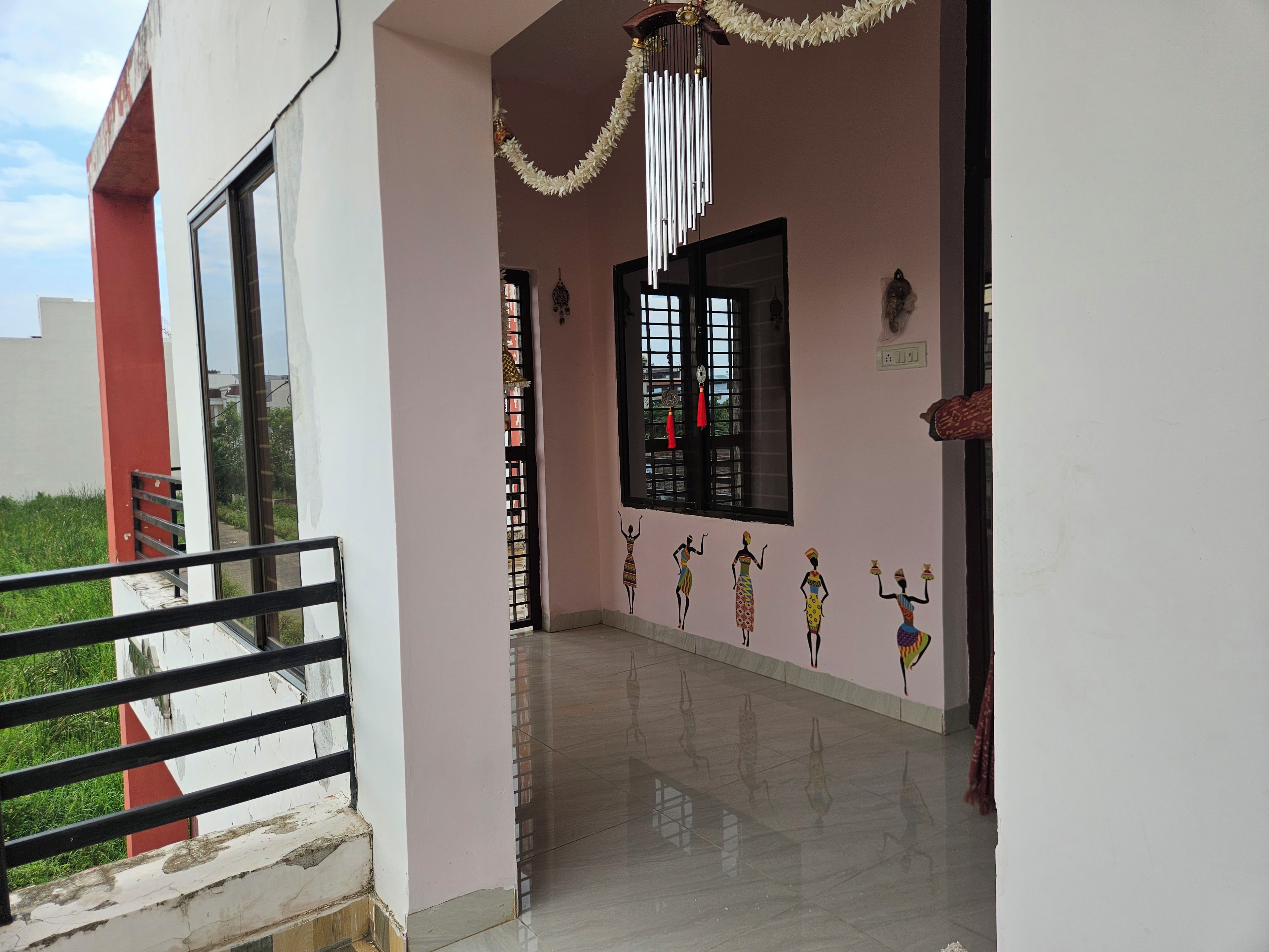 Um corredor com piso de azulejos, janela com moldura preta e parede com obras de arte.