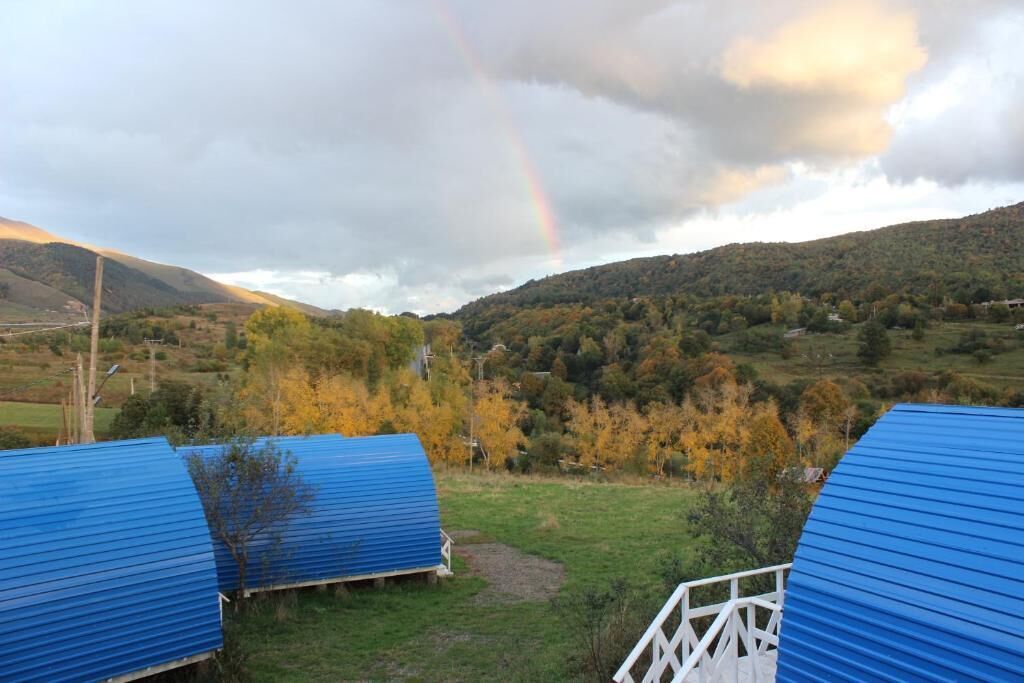 A rural landscape with blue-roofed structures, a rainbow, and autumn-colored trees.