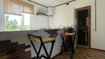 Una cocina con piso en patrón de espiga, una ventana con persianas y una puerta que da a otra habitación.