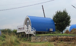 A blue-roofed structure with a white staircase leading to a door, set on a stone base with hay bales nearby.