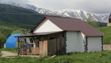 A small, single-story building with a corrugated metal roof, situated in a rural area with mountains in the background.