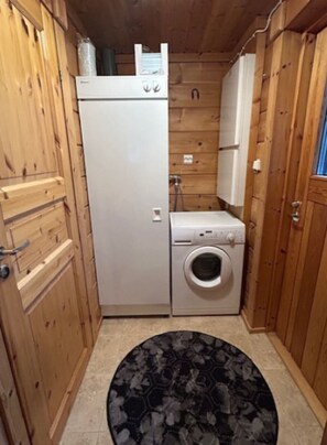 A compact laundry room with a washing machine and dryer, wooden cabinets, and a patterned rug on the floor. - Nietos B | Pet-Friendly Cabin with Private Sauna (Kuusamo)