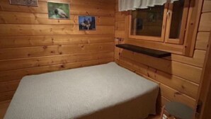 Ein kleines Zimmer mit einem Einzelbett, Holzwänden und einem Fenster mit Vorhang.
