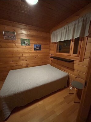 A small, single-bed room with wooden walls and a window with a curtain. - Nietos B | Pet-Friendly Cabin with Private Sauna (Kuusamo)