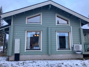 A two-story house with a gabled roof, large windows, and an air conditioning unit mounted on the exterior wall. - Nietos B | Pet-Friendly Cabin with Private Sauna (Kuusamo)