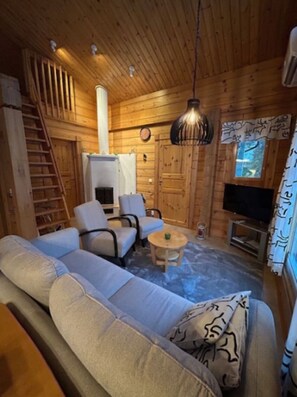 A cozy cabin interior with a sofa, chairs, a table, a fireplace, a television, and a wooden staircase. - Nietos B | Pet-Friendly Cabin with Private Sauna (Kuusamo)