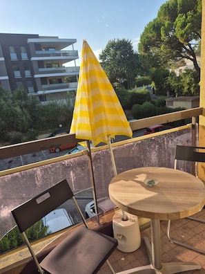 A balcony with a yellow striped umbrella, a round wooden table, and chairs. - Charming, very bright one-bedroom apartment (Villeneuve-Loubet)