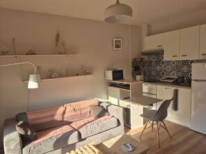 A compact living space with a kitchenette, a sofa, a dining table, and a lamp. - Charming, very bright one-bedroom apartment (Villeneuve-Loubet)