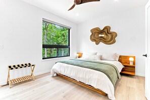 Ein Schlafzimmer mit einem großen Fenster, einem Bett mit Holz-Kopfteil, einem Heizkörper und einer Wandleuchte.