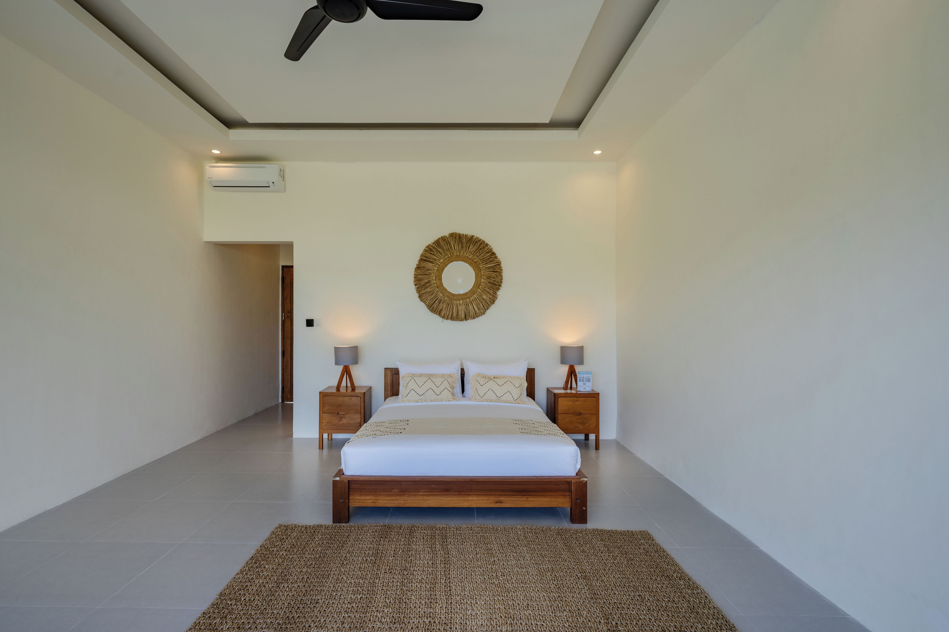 Een slaapkamer met een bed, nachtkastjes, een wandairconditioner, een plafondventilator en een decoratief object aan de muur.