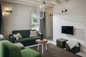 A modern living room with a green sofa, a round wooden side table, and a television mounted on the wall. - Lodge in Schaijk with Garden Terrace (Schaijk)