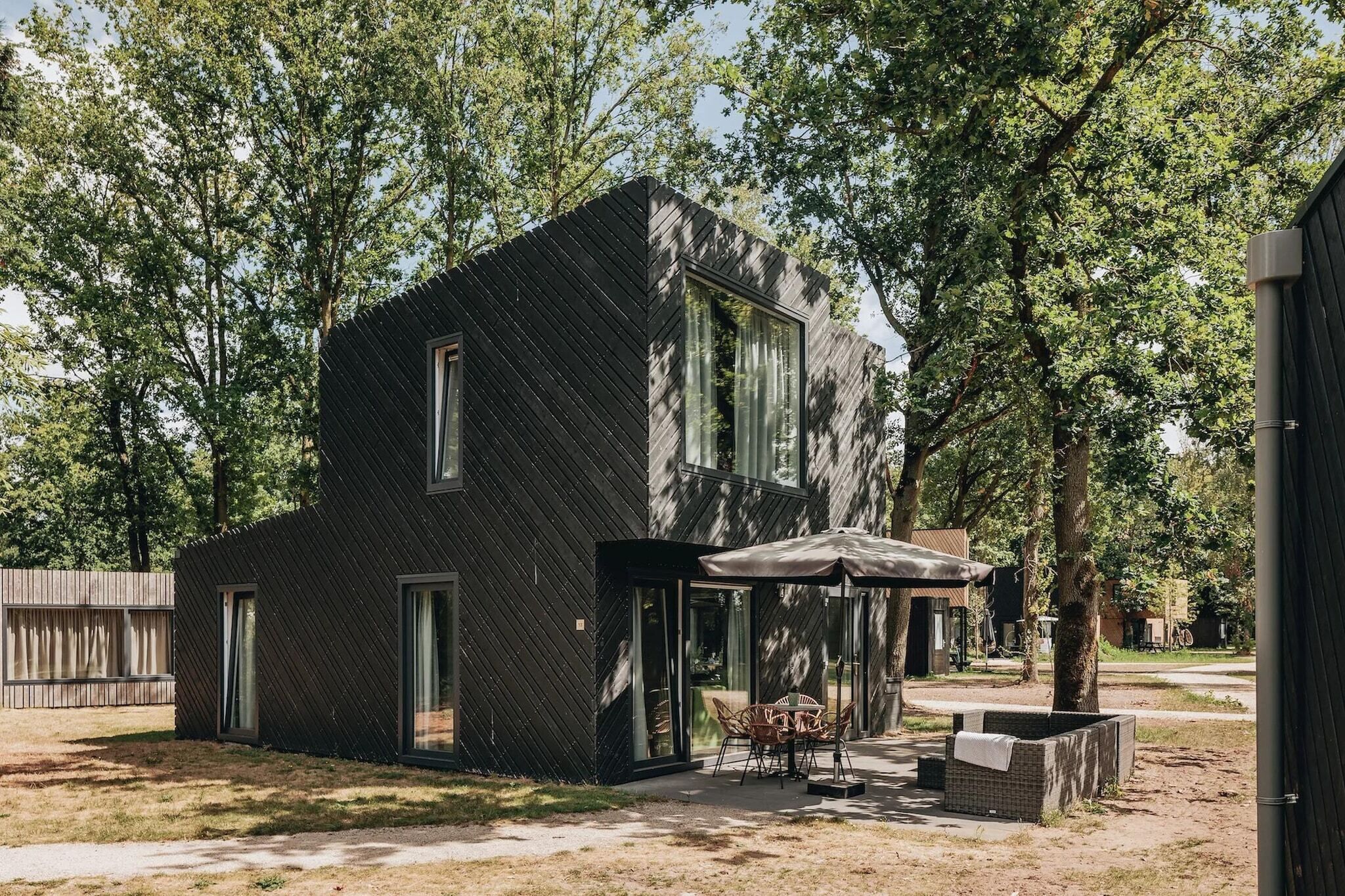 Un edificio moderno a due piani con tetto spiovente, ampie finestre e un patio arredato con mobili da esterno.