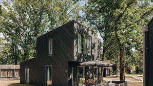Een modern gebouw met twee verdiepingen, een schuin dak, grote ramen en een patio met tuinmeubilair.