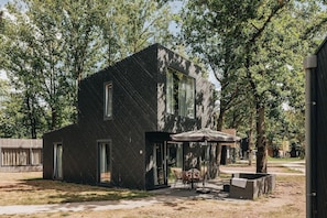 A modern two-story building with a sloped roof, large windows, and a patio area with outdoor furniture. - Lodge in Schaijk with Garden Terrace (Schaijk)