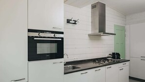 Een moderne keuken met witte kasten, een zwarte oven, een roestvrijstalen afzuigkap en een groene deur.