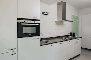 A modern kitchen with white cabinetry, a black oven, a stainless steel range hood, and a green door. - Lodge in Schaijk with Garden Terrace (Schaijk)