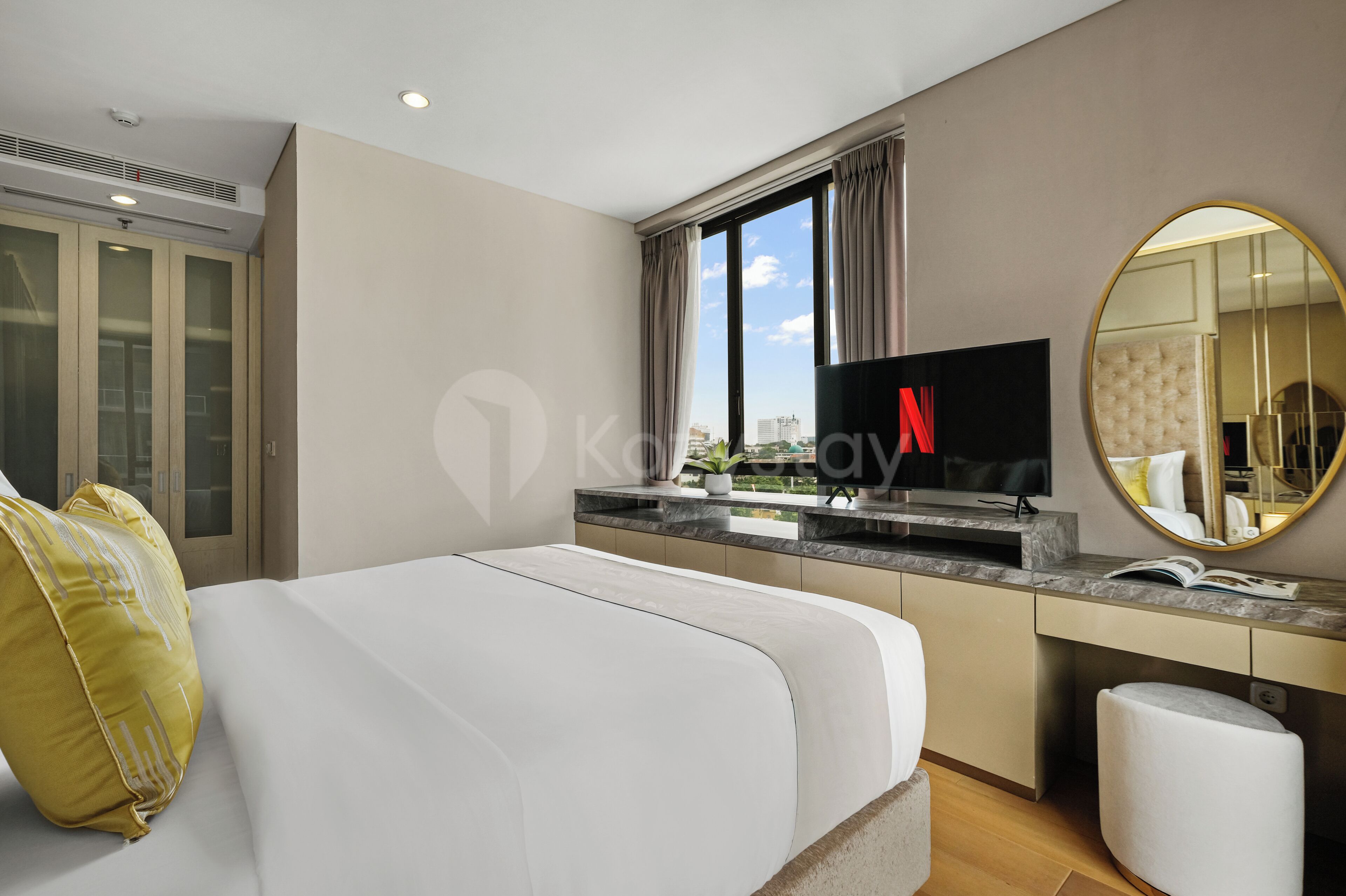 A hotel room with a bed, a TV, a desk, a mirror, and a window with a view of the city.
