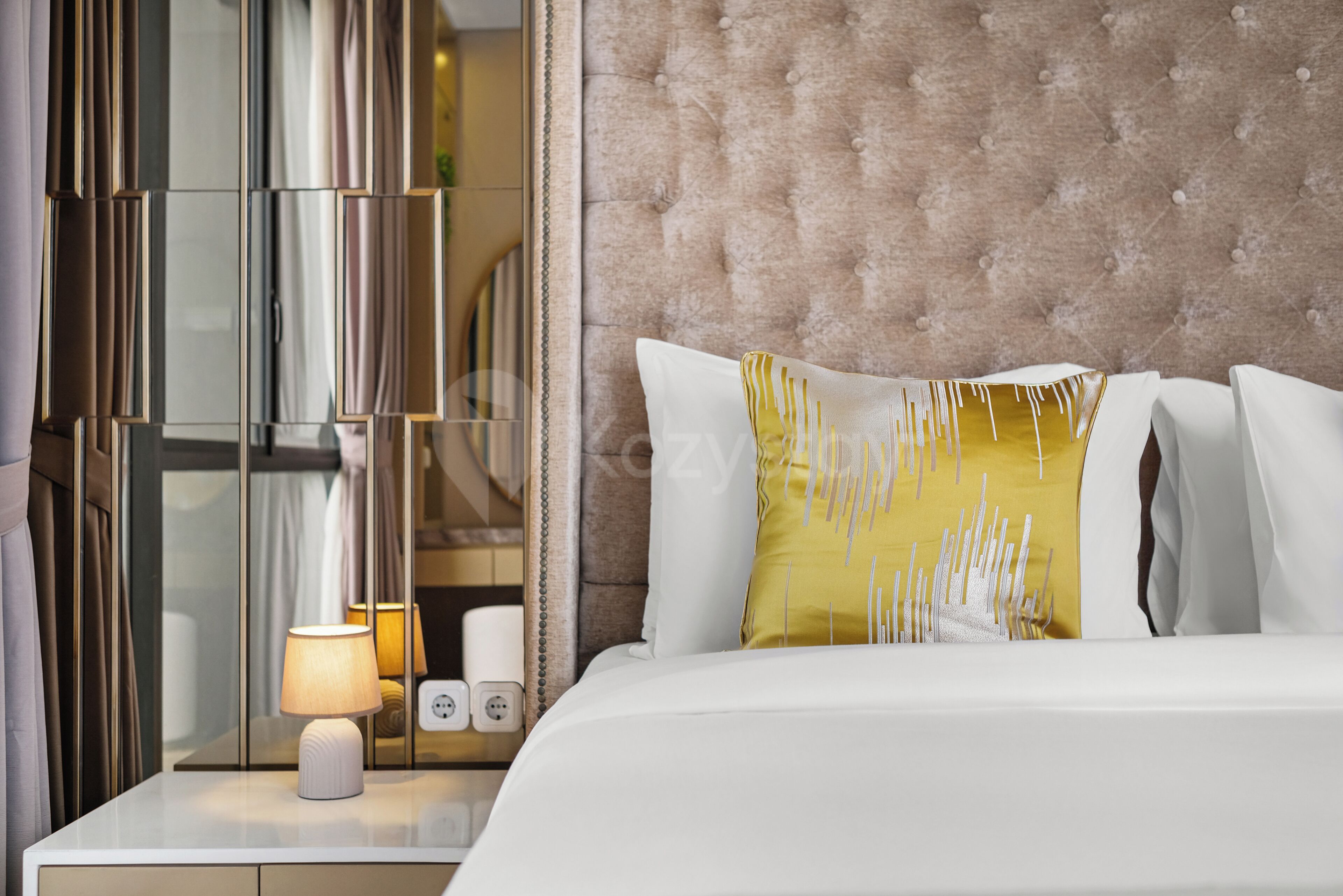 A hotel room with a bed, a nightstand with a lamp, and a mirror.