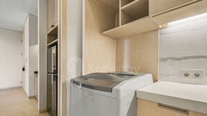 A compact kitchen with a built-in washer and dryer, wooden cabinets, and a marble backsplash. - Anera by Kozystay - Cilandak (South Jakarta)
