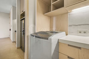 A compact kitchen with a built-in washer and dryer, wooden cabinets, and a marble backsplash. - Anera by Kozystay - Cilandak (South Jakarta)