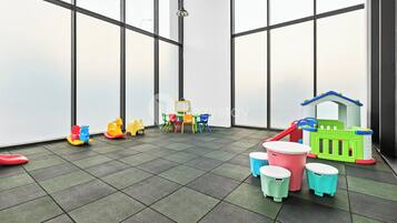 A children's play area with a green playhouse, colorful chairs, and a small table.