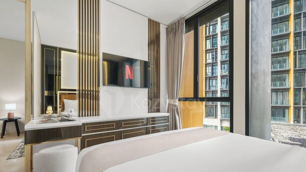 A modern hotel room with a large bed, a flat-screen TV mounted on the wall, a desk with a chair, and a view of a building through the window. - Anera by Kozystay - Cilandak (South Jakarta)