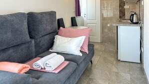 A grey sofa with rolled towels and pillows, a white door, and a kitchen area with a kettle. - Lovely apartment in Rogoznica with WiFi (Rogoznica)
