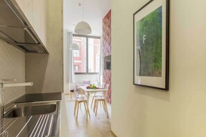 Uma cozinha moderna com uma pia de aço inoxidável, uma área de refeições com mesa e cadeiras, e uma obra de arte emoldurada na parede.