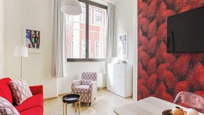 Ein modernes Wohnzimmer mit einem roten Sofa, einem gemusterten Sessel und einem Esstisch.