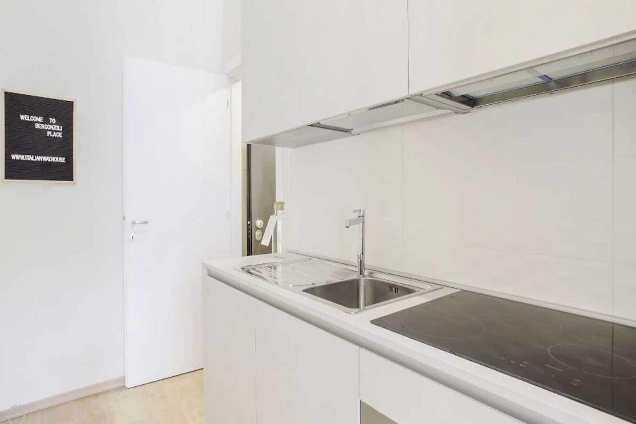 A modern kitchen with a stainless steel sink, a white countertop, and a black backsplash.