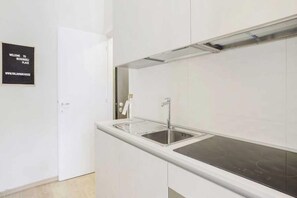 Uma cozinha moderna com uma pia de aço inoxidável, bancada branca e painel de parede preto.