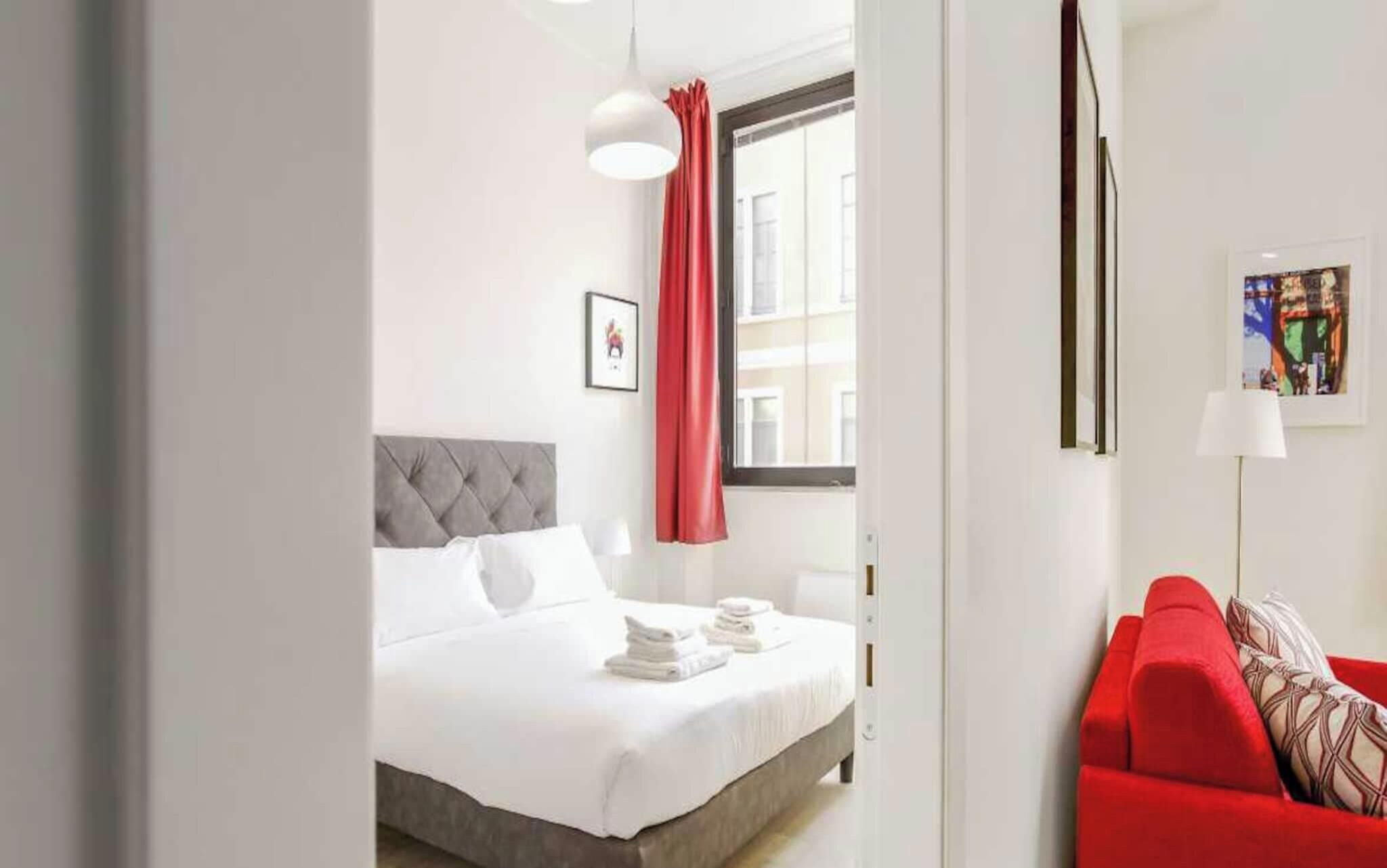 Ein Hotelzimmer mit einem Bett, einem roten Sofa, einem Fenster mit Vorhängen und einem Gemälde an der Wand.