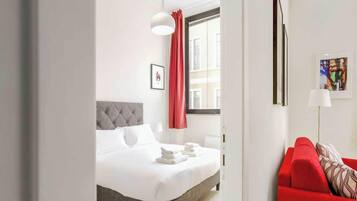 Ein Hotelzimmer mit einem Bett, einem roten Sofa, einem Fenster mit Vorhängen und einem Gemälde an der Wand.
