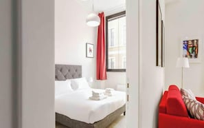 A hotel room with a bed, a red sofa, a window with curtains, and a painting on the wall. - Charming Apartment 2BR/5P - Milano Centrale (Milano)