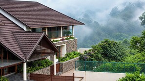A modern two-story house with a sloped roof, large windows, and a balcony with plants. - Olive Woods (Devikolam)