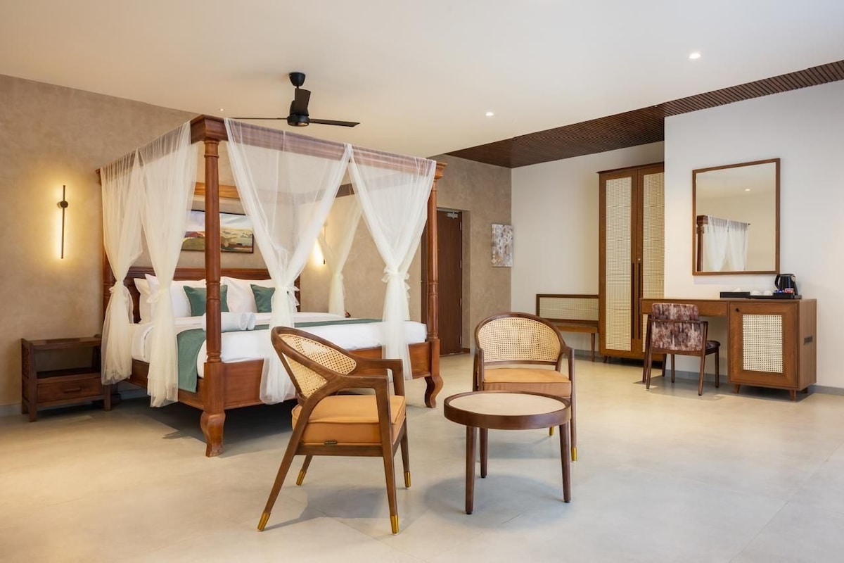 A bedroom with a four-poster bed, two chairs, a desk, and a mirror.