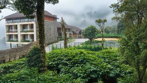 A hotel with multiple floors, balconies with plants, and a view of a lush garden and distant hills. - Olive Woods (Devikolam)