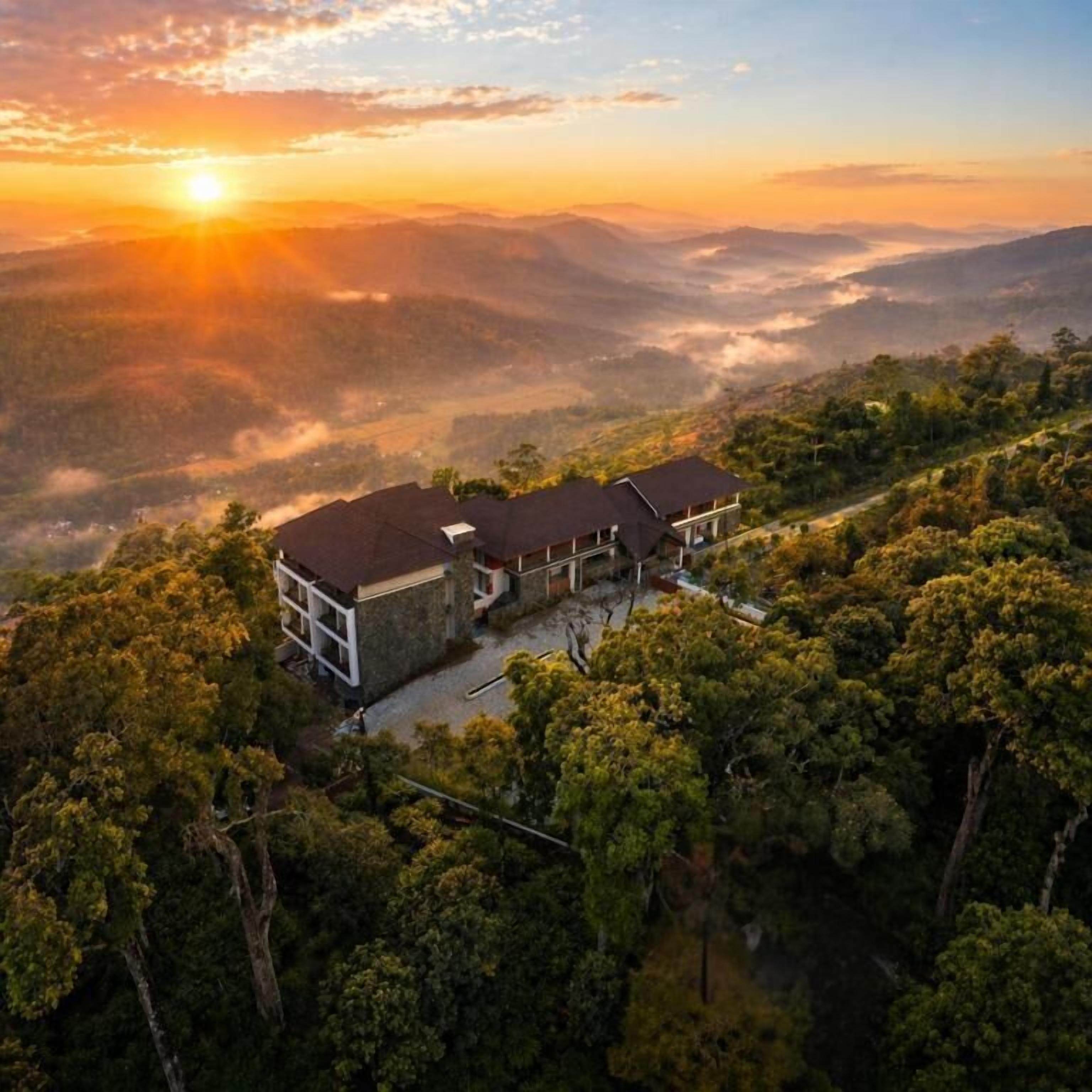 Un edificio de dos plantas con techo plano, rodeado de un bosque denso y con vistas a colinas distantes.
