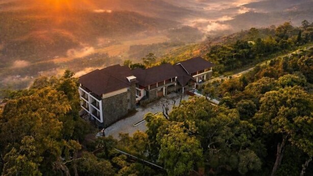 A two-story building with a flat roof, surrounded by dense forest, and a view of distant hills. - Olive Woods (CHINNAKANAL)
