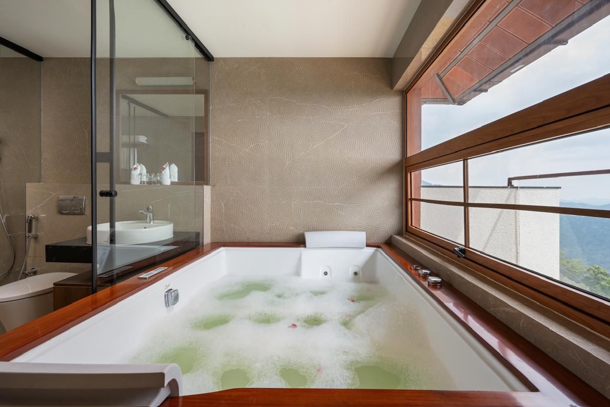 A modern bathroom with a large bathtub, a glass shower enclosure, and a view of the outdoors.