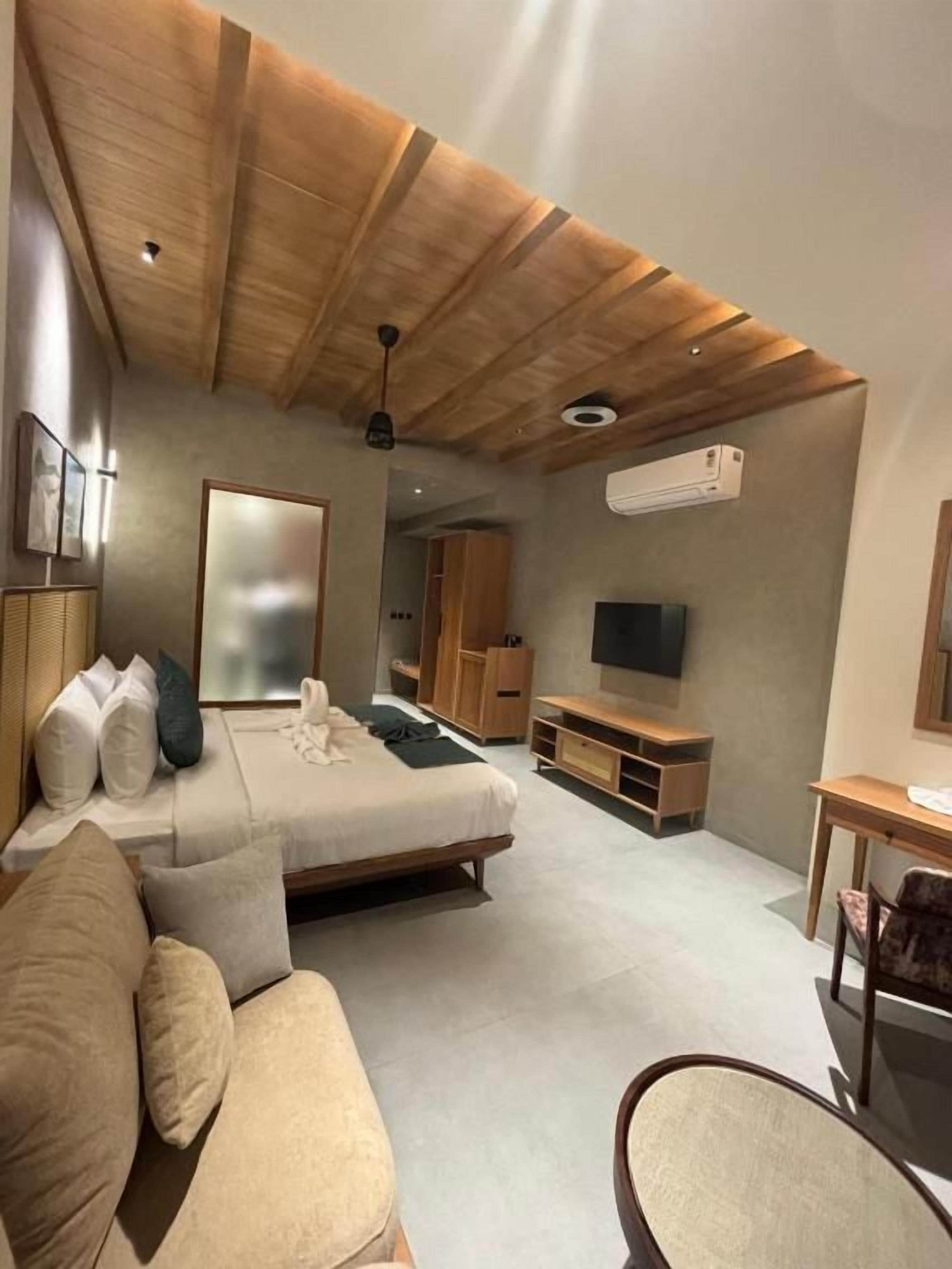 Een moderne slaapkamer met een houten plafond, een bed, een bank, een televisie en een bureau.