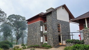 A two-story building with a stone facade, a red roof, and a staircase leading to the upper floor. - Olive Woods (Devikolam)