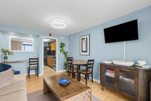 A modern living room with a dining area, a flat-screen TV mounted on the wall, and a kitchen in the background. - Fifth-Floor Oceanfront Retreat | King Bed (Myrtle Beach)