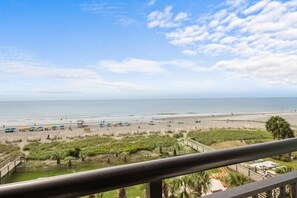 A beach view from a balcony with a railing, a sandy beach, and a clear sky. - Fifth-Floor Oceanfront Retreat | King Bed (Myrtle Beach)