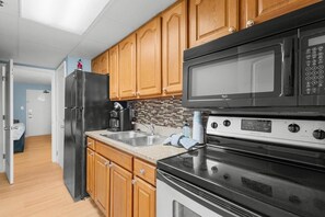 A kitchen with wooden cabinets, a stainless steel refrigerator, a microwave, and an oven. - Fifth-Floor Oceanfront Retreat | King Bed (Myrtle Beach)