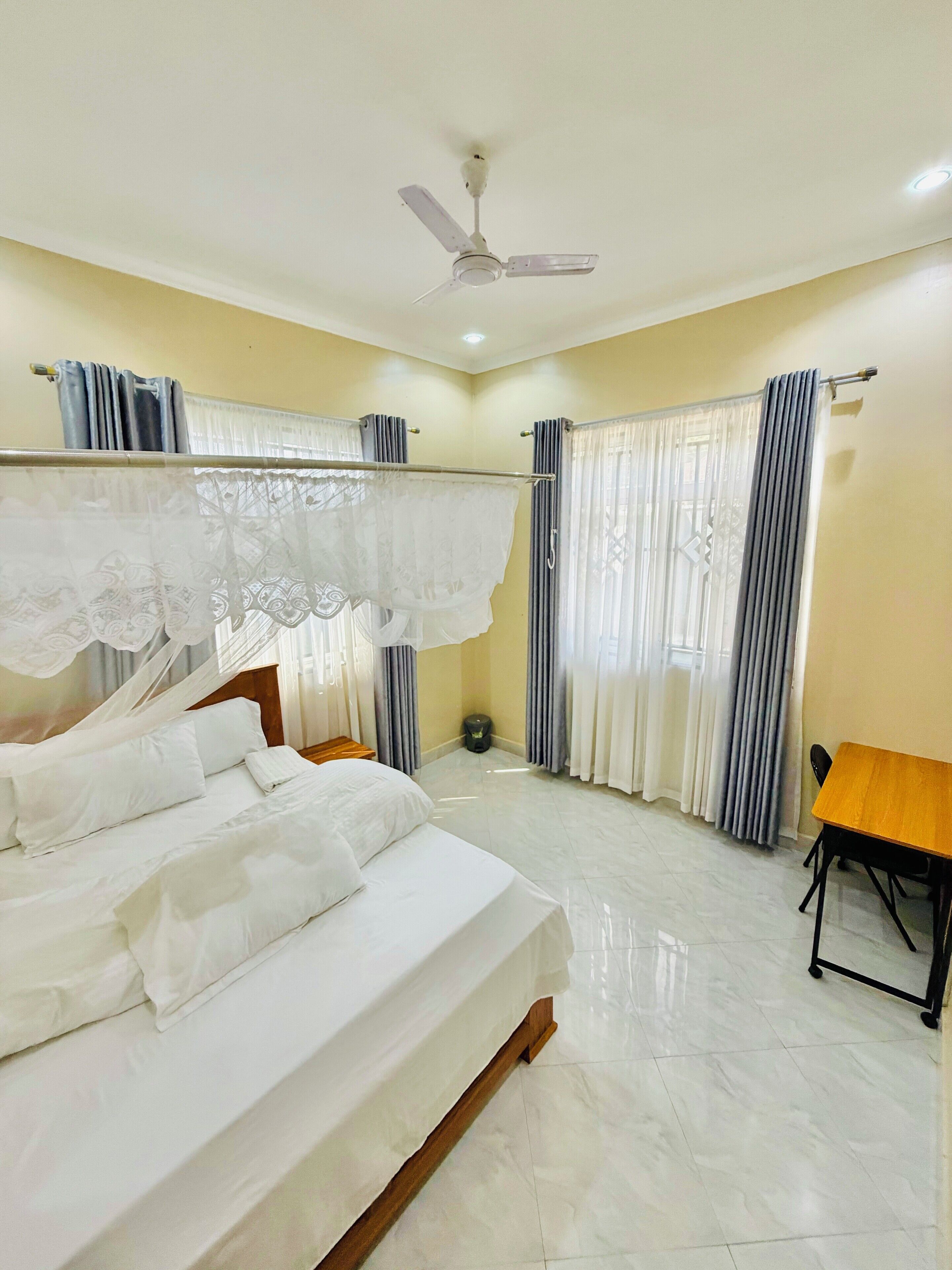 A bedroom with a bed, a ceiling fan, a table, and curtains.
