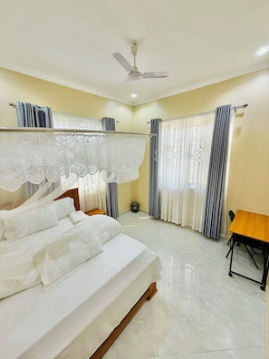 A bedroom with a bed, a ceiling fan, a table, and curtains.