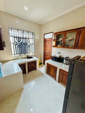 A kitchen with white marble countertops, wooden cabinets, a stainless steel refrigerator, and a window with decorative metal bars.